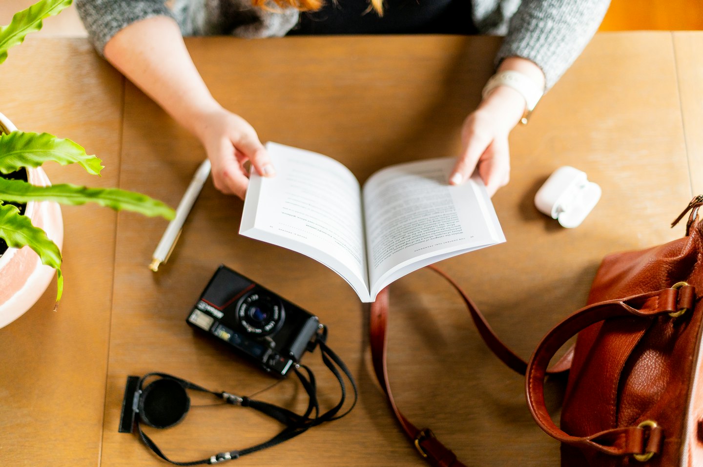 Hands hold an open book on a desk with accessories.