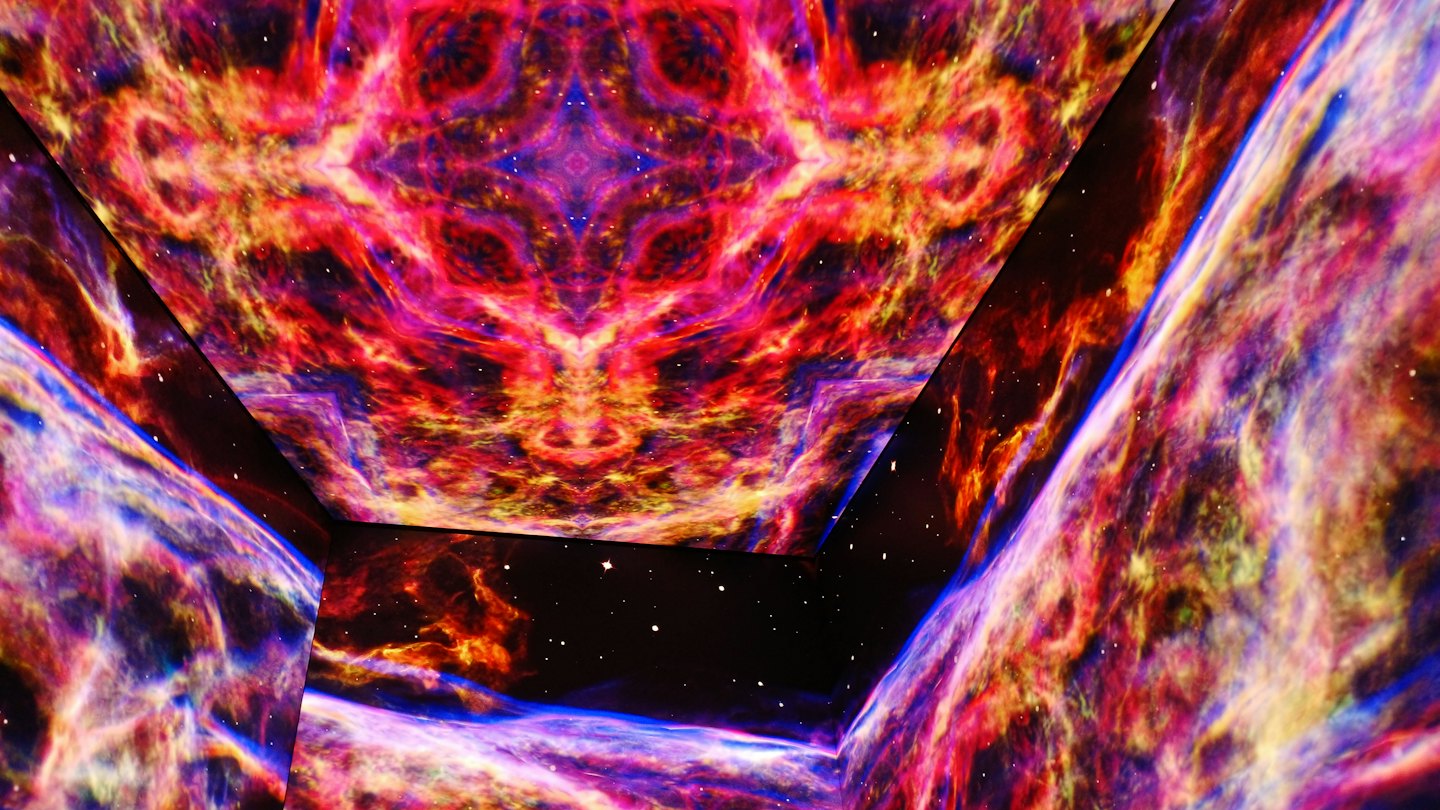 Abstract cosmic light patterns project onto angled gallery walls.